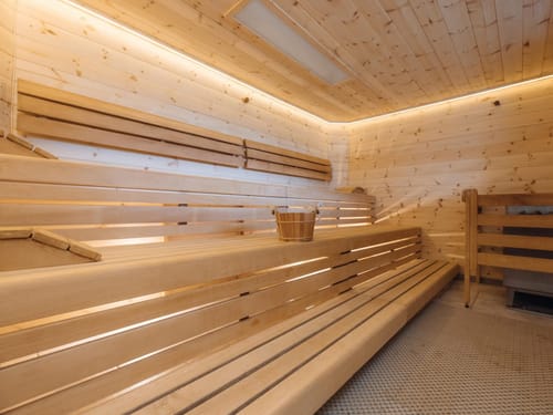 Moderne Holzsauna mit warmem Licht und Eimer auf der Bank