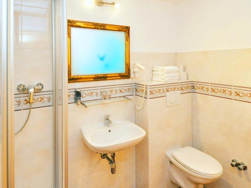 Badbereich mit Badewanne, Wandspiegel, Föhn und gläsernen Waschtisch