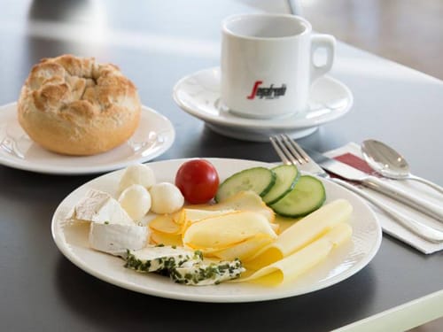Frühstücksteller mit einer Auswahl an Käse und Gurke und Tomate, Brötchen und einer Tassen Kaffee