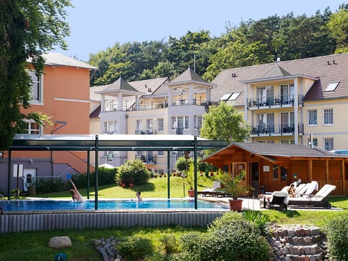 Bick auf das Hotel und den Pool mit Liegewiese im Garten