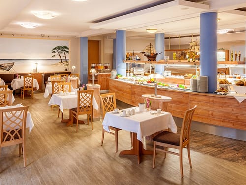 Frühstücksraum mit eingedeckten Tischen und einem Speisenbuffet