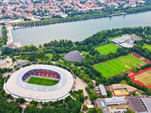 Luftaufnahme eines Stadions und umliegender Parklandschaft an einem See