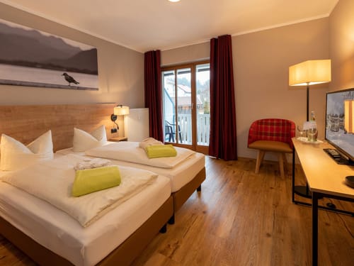 modernes Doppelzimmer in Holzoptik mit Doppelbett, Sessel, Stehlampe, TV und Schreibtisch