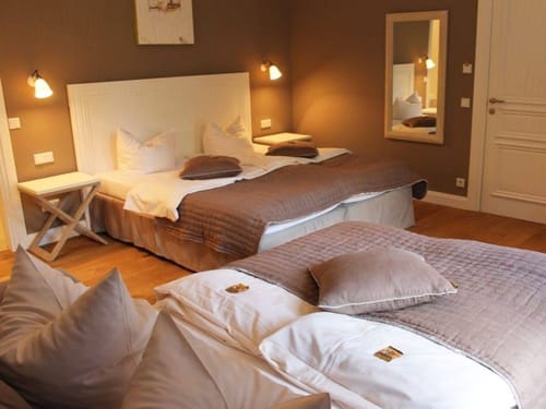 zwei Boxspringbetten mit kleinen Tischen und Wandspiegel im Mehrbettzimmer