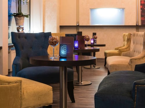 Hotel-Lounge mit eleganten Sesseln, dekorativen Tischlampen und Speisekarten auf runden Holztischen