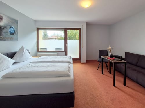 geräumiges Doppelzimmer mit Doppelbett, kleinen Tisch, Stuhl, Couch und Balkon