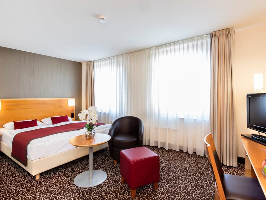 Doppelzimmer mit Doppelbett, Sessel, Hocker, TV und Schreibtisch