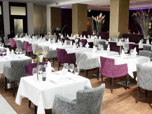 Hotelrestaurant mit weiß eingedeckten Tischen und farbigen Stühlen