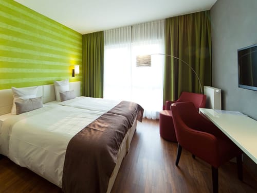 Komfortables Doppelzimmer mit modernem Design, grüner Tapete und roten Akzentstühlen