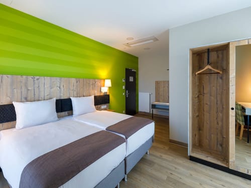 Komfortables Doppelzimmer mit grüner Designwand, Holzelementen und moderner Einrichtung