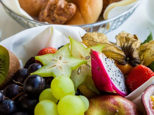 Frische exotische Früchte auf einem Tisch, darunter Drachenfrucht, Sternfrucht, Trauben, Physalis und Kiwis.