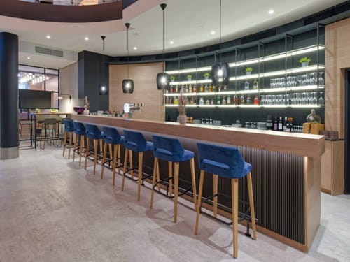 Moderne Hotelbar mit blauen Barhockern und gut beleuchteten Regalen mit Spirituosen.