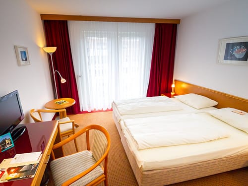 Doppelzimmer mit Doppelbett, TV, zwei Stühlen und Tisch