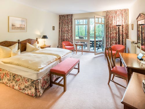 großzüges Doppelzimmer mit Doppelbett, Sesseln, Schreibtisch, Stuhl und Balkon