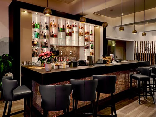 Elegante moderne Bar mit beleuchtetem Flaschenregal und stilvollen Pendelleuchten