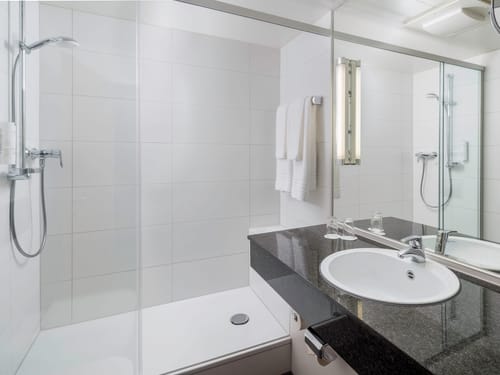 Badbereich mit Dusche, großem Wandspiegel und Waschtich