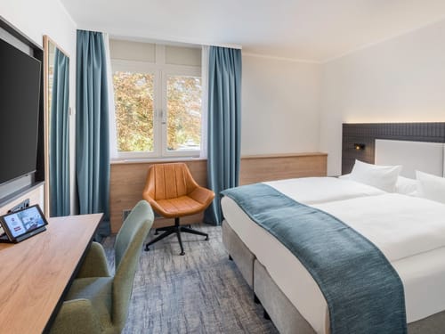 Doppelzimmer Standard mit Doppelbett, Sessel, Stuhl, TV und Schreibtisch