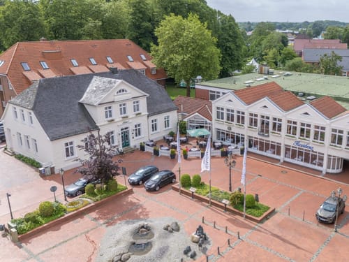 Luftaufnahme eines historischen Gebaeudes und eines modernen Restaurants in einer Stadt mit Kopfsteinpflasterplatz und Springbrunnen.