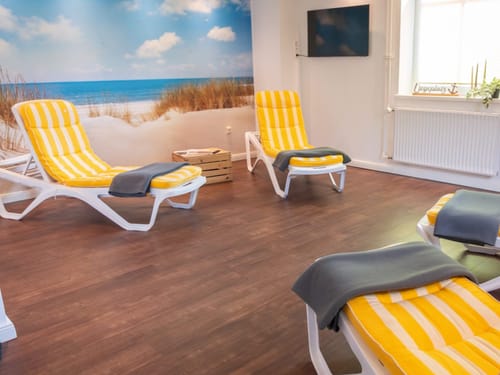 Entspannungsraum mit gelb-weiß gestreiften Liegestuehlen vor einem Strandhintergrund