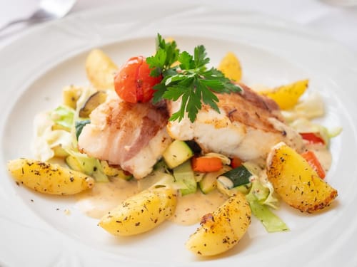 Gebratenes Fischfilet mit Speck, serviert mit gerösteten Kartoffeln und buntem Gemuese