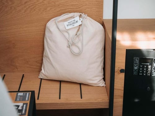 Leinensack auf Holztisch mit der Aufschrift "Frisch zum Kuscheln" neben einem Safe.