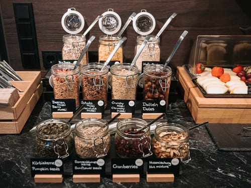 Müsli-Bar mit verschiedenen Bio-Produkten in Glasbehältern, darunter Beeren-Müsli, Schoko-Müsli, Datteln und Nussmischungen.