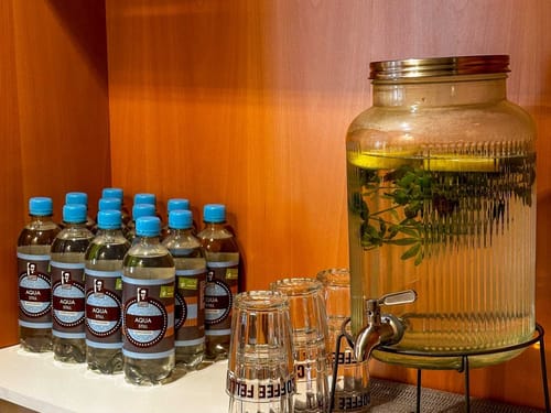 Wasserflaschen und ein Spender mit Zitronen-Minz-Wasser auf einem Regal.