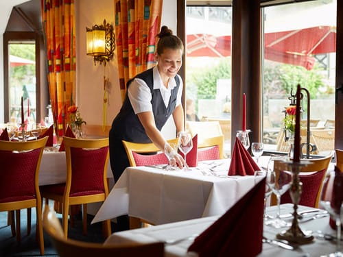 Eine Servicemitarbeiterin deckt im Restaurant die Tische ein