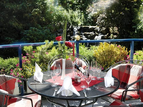 Eleganter Gartenterrassen-Tisch mit gedecktem Gedeck und umgeben von blühenden Pflanzen.