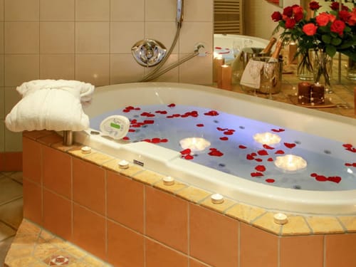 Luxuriöses Badezimmer mit Whirlpool, umgeben von Kerzen und Rosenblättern.