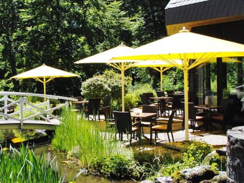 Garten und Hotelterrasse mit Sonnenschirmen, Gartenmöblen und kleiner Tecihbrücke