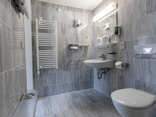 Entdecken Sie ein stilvolles, modernes Badezimmer mit grauen Fliesen, einem wandmontierten Waschbecken und einer schlichten Toilette. Perfekt für elegante und funktionale Badezimmerdesigns.