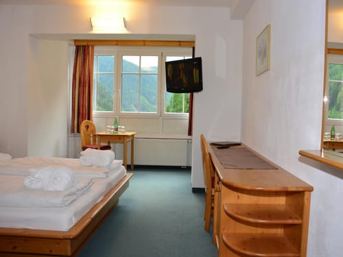 Gemütliches Hotelzimmer mit Doppelbett, TV, Schreibtisch und Bergblick durch das Fenster.