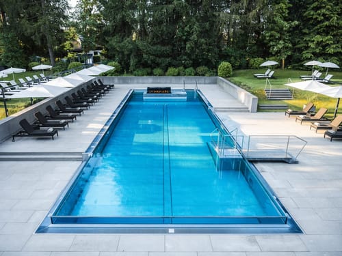 Weitläufige Außenpoolanlage mit elegantem Design, Relaxzone und natürlicher Gartenatmosphäre