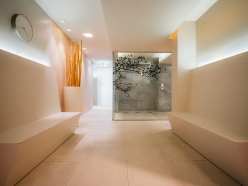 Stilvoll gestalteter Spa-Korridor mit beleuchtetem Glasdampfbad, Naturdekor und warmer Ambientebeleuchtung für höchsten Entspannungskomfort
