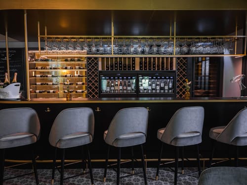 Bar mit stimmungsvoller Beleuchtung, umfangreichem Getränkesortiment und eleganten Barhockern