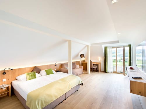 großzügiges Doppelzimmer mit Doppelbett, Couch. Schreibtisch, Stehlampe und Stuhl