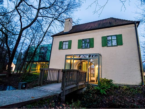 Eingang des MK Schlossparkhotel mit Brücke und beleuchtetem Foyer