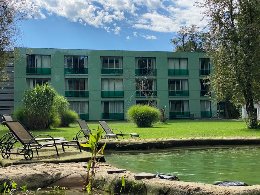 Hotelansicht bei Sonnenschein mit Garten, Teich und Liegestühle