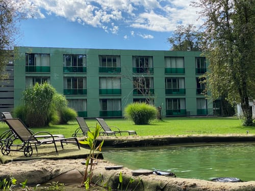 Hotelansicht bei Sonnenschein mit Garten, Teich und Liegestühle