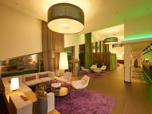 Lobby mit Loungemöbeln, Sesseln, Rezeption und großen Deckenleuchten