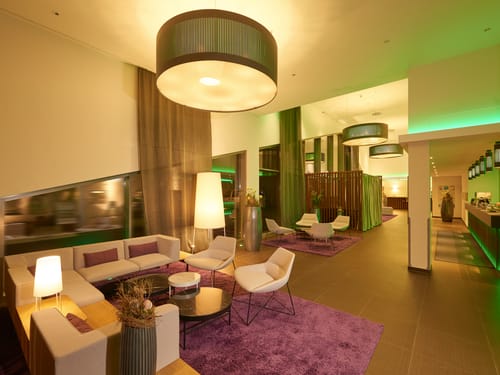 Lobby mit Loungemöbeln, Sesseln, Rezeption und großen Deckenleuchten