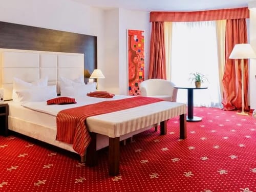 Komfort Doppelzimmer mit rotem Teppich, Doppelbett, Sessel und Stehlampe