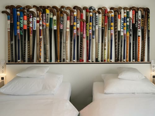 Sammlung von Vintage-Hockeyschlägern über zwei weißen Betten in einem Hotelzimmer.