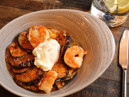 Schüssel mit gebratenen Garnelen, Zucchini und einer Creme auf Holztisch