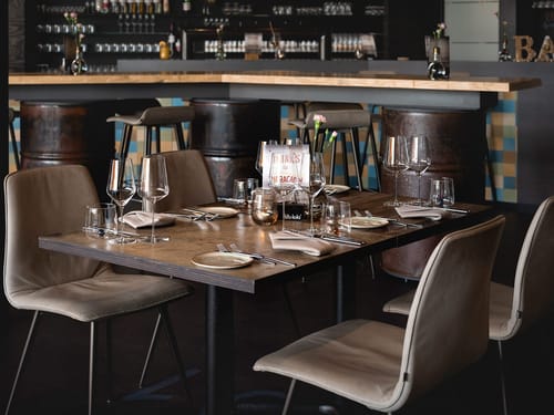 Elegantes Restaurantinterieur mit gedecktem Tisch und modernen Barhockern im Hintergrund.