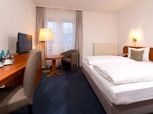 Zweibettzimmer mit Sesseln, TV Schreibtisch und Stehlampe