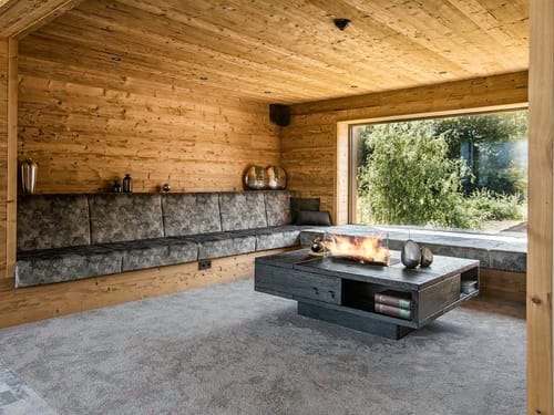 große Sitzbank und Tisch mit Kaminfeuer sowie Panoramafenster
