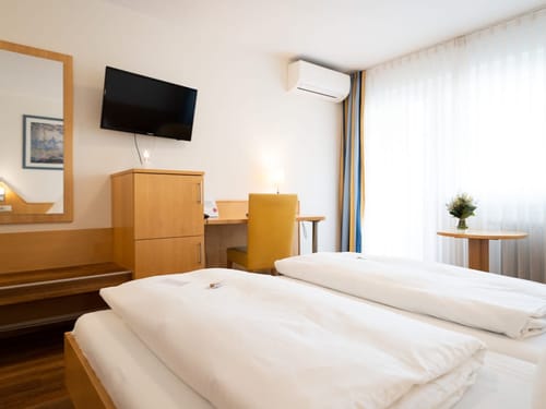 Helles Hotelzimmer mit Schreibtisch, Fernseher und großen Fenstern