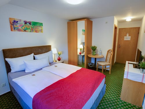 einfaches Zimmer mit Doppelbett, Wandschrank, Tisch und Stuhl